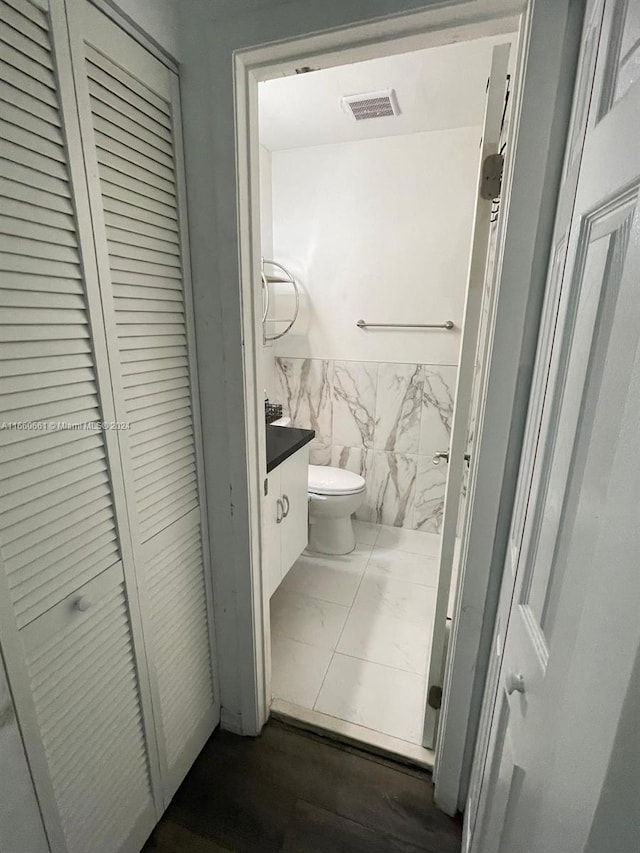 bathroom featuring wood-type flooring, vanity, tile walls, and toilet