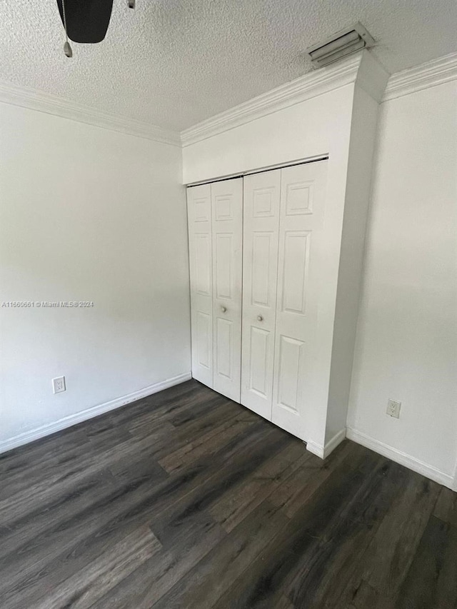 unfurnished bedroom with a textured ceiling, crown molding, dark wood-type flooring, and a closet