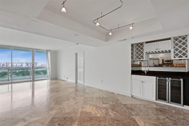 bar featuring rail lighting, a water view, crown molding, a tray ceiling, and beverage cooler