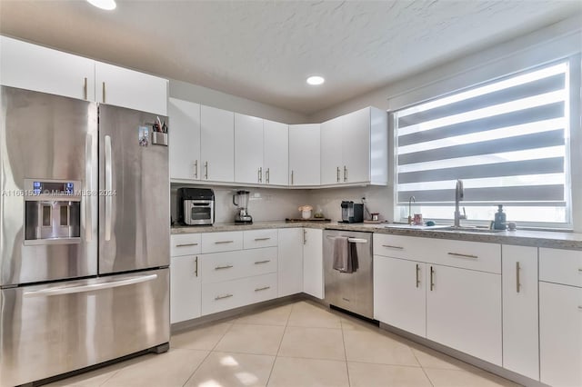 kitchen with light stone counters, a textured ceiling, light tile patterned flooring, white cabinetry, and appliances with stainless steel finishes