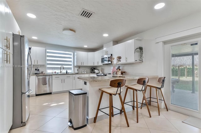 kitchen with stainless steel appliances, kitchen peninsula, a kitchen breakfast bar, and white cabinetry