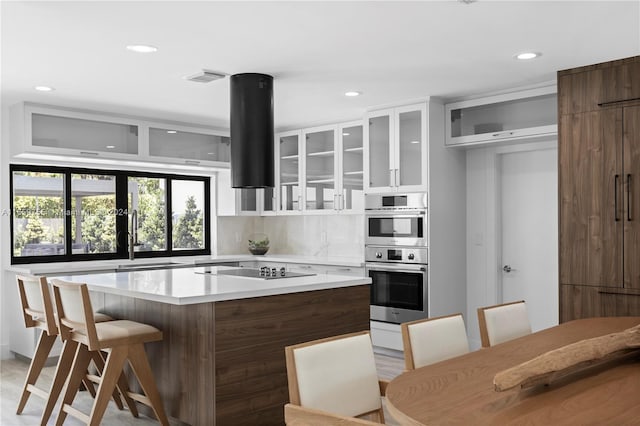 kitchen featuring a center island, stainless steel double oven, backsplash, a breakfast bar area, and black electric stovetop