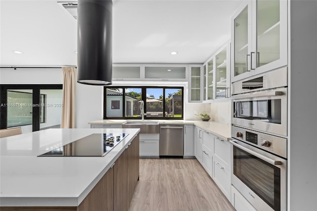 kitchen with white cabinets, a sink, light countertops, light wood finished floors, and stainless steel appliances