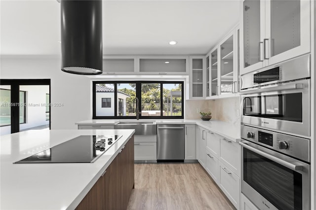 kitchen with appliances with stainless steel finishes, backsplash, sink, white cabinets, and light hardwood / wood-style floors