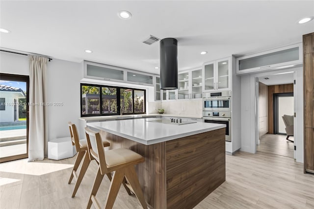 kitchen with double oven, visible vents, a kitchen island, light countertops, and island range hood