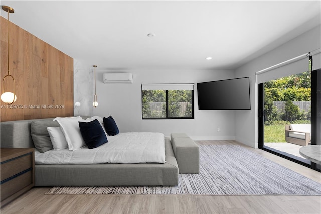 bedroom featuring a wall mounted air conditioner, access to outside, light hardwood / wood-style flooring, and multiple windows