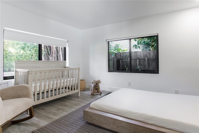 bedroom featuring multiple windows, a crib, and hardwood / wood-style flooring