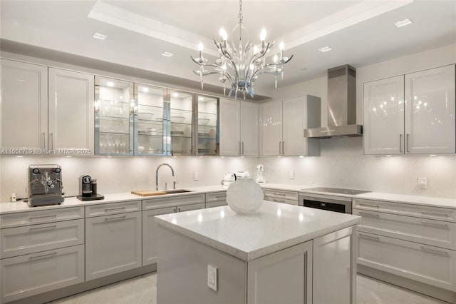 kitchen featuring a tray ceiling, wall chimney exhaust hood, backsplash, and a sink