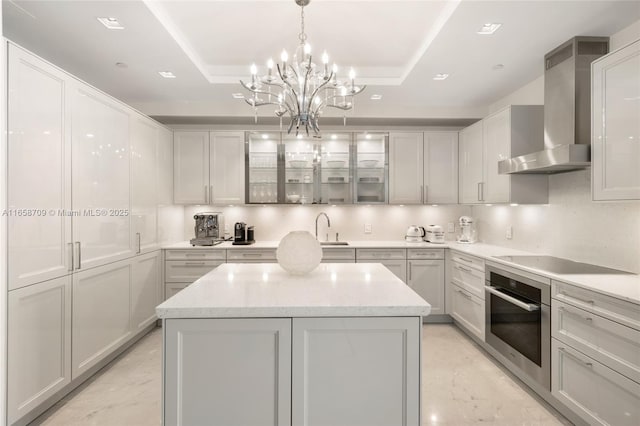 kitchen with stainless steel oven, a tray ceiling, black electric stovetop, and wall chimney exhaust hood