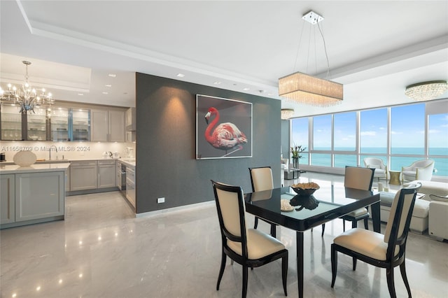 kitchen with a tray ceiling, a center island, sink, wall chimney exhaust hood, and decorative light fixtures