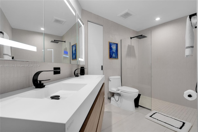 bathroom with tile walls, tiled shower, vanity, toilet, and tile patterned floors