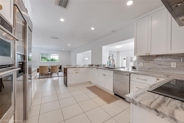 kitchen with sink, white cabinetry, kitchen peninsula, appliances with stainless steel finishes, and light stone countertops