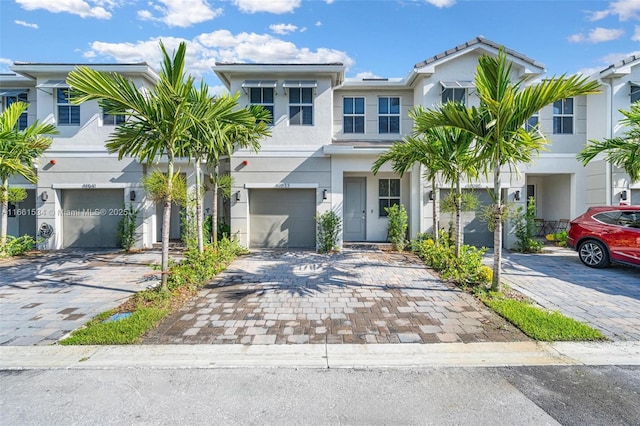 townhome / multi-family property with decorative driveway, a garage, and stucco siding