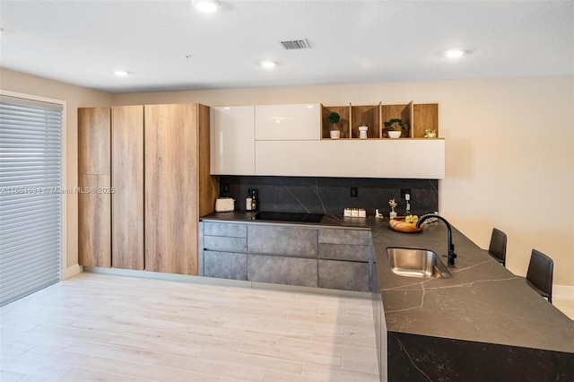 kitchen featuring visible vents, a sink, open shelves, dark countertops, and black electric cooktop