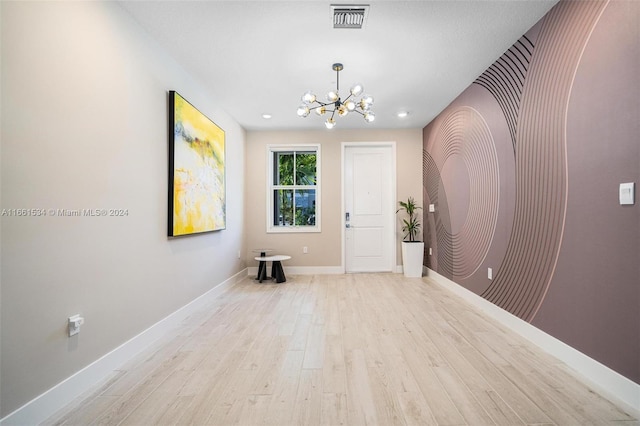 empty room with a notable chandelier and light wood-type flooring