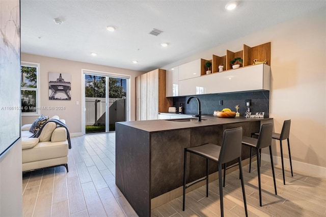 kitchen featuring white cabinets, sink, light hardwood / wood-style flooring, a breakfast bar area, and decorative backsplash