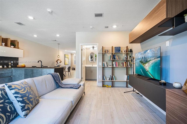 living room featuring a textured ceiling, light wood-type flooring, and sink