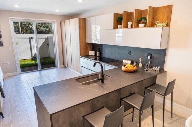 kitchen with light hardwood / wood-style floors, tasteful backsplash, white cabinets, black electric stovetop, and sink