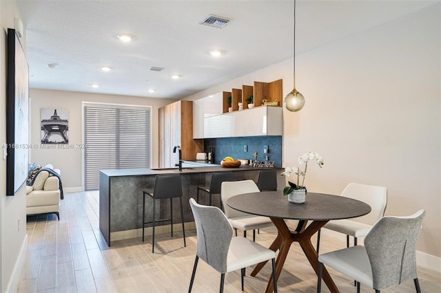 kitchen with white cabinets, kitchen peninsula, light hardwood / wood-style flooring, decorative light fixtures, and a breakfast bar