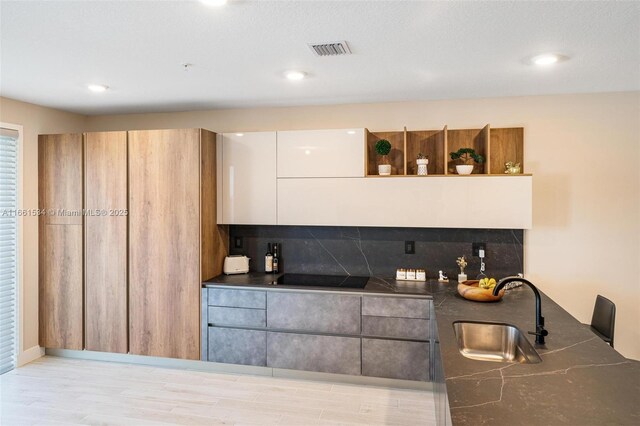 kitchen with white cabinets, sink, black stovetop, light wood-type flooring, and decorative backsplash