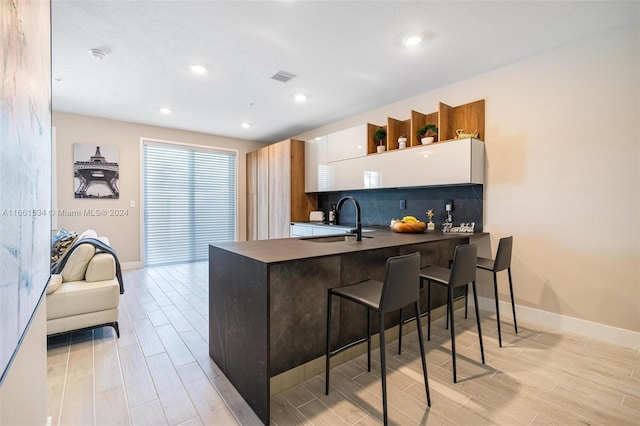 kitchen with white cabinets, sink, kitchen peninsula, tasteful backsplash, and light hardwood / wood-style floors