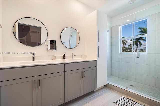 full bath with a sink, double vanity, wood finished floors, and a shower stall