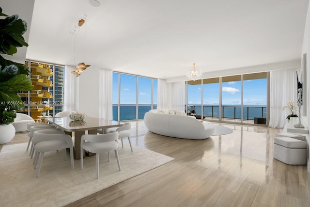 dining room featuring light wood-type flooring, a water view, expansive windows, and a chandelier