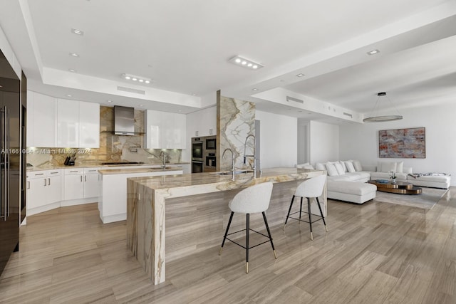 kitchen featuring a kitchen breakfast bar, decorative backsplash, white cabinets, a large island, and wall chimney range hood