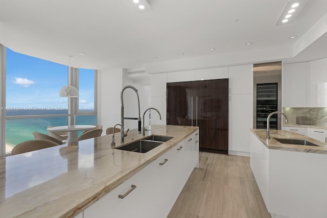 kitchen with white cabinets, pendant lighting, light wood-type flooring, a water view, and decorative backsplash