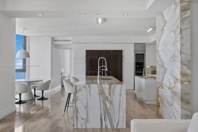 kitchen featuring light wood-type flooring, sink, white cabinetry, a center island with sink, and light stone countertops