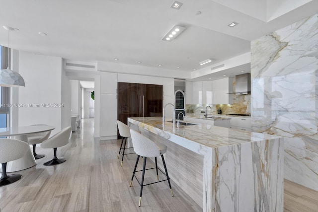 kitchen with white cabinets, sink, a large island, light hardwood / wood-style flooring, and wall chimney range hood