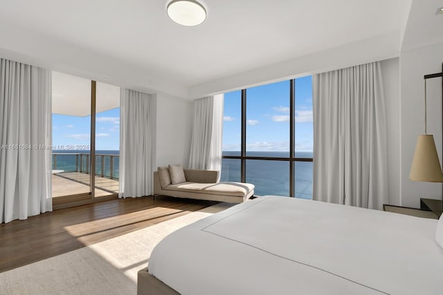 bedroom with multiple windows, a water view, hardwood / wood-style floors, and access to exterior