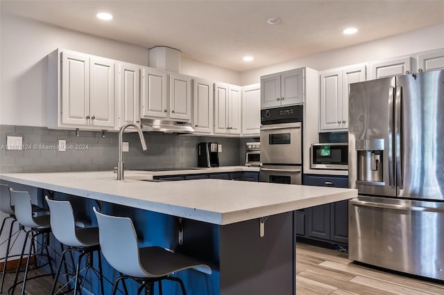 kitchen with white cabinetry, a kitchen breakfast bar, light hardwood / wood-style flooring, backsplash, and appliances with stainless steel finishes