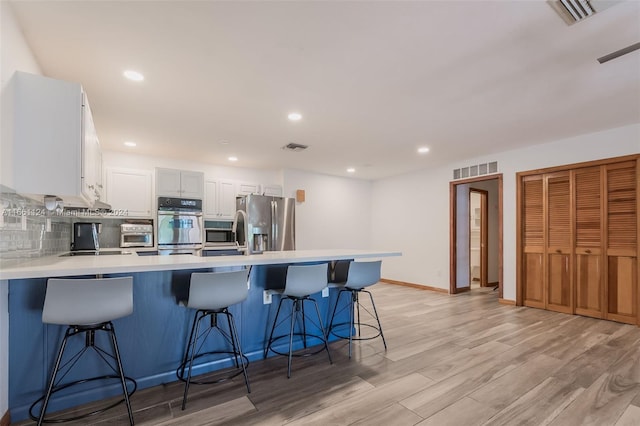 kitchen featuring light wood-type flooring, stainless steel refrigerator with ice dispenser, white cabinetry, and a kitchen breakfast bar