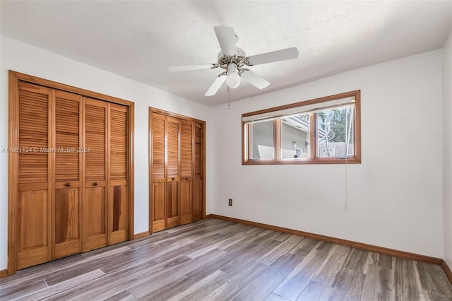 unfurnished bedroom featuring light hardwood / wood-style floors, ceiling fan, and multiple closets