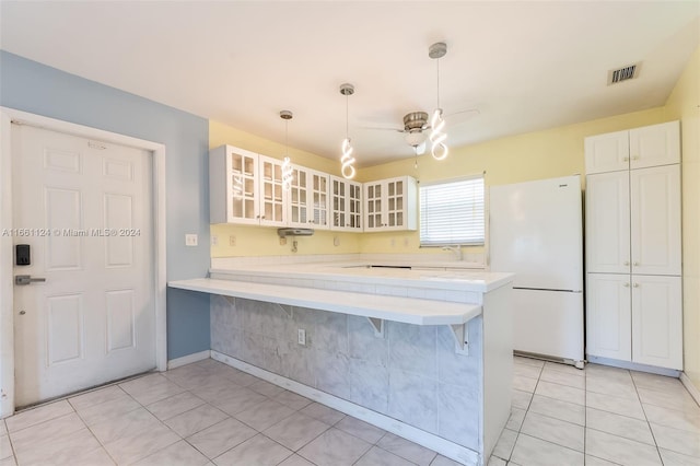 kitchen featuring hanging light fixtures, white cabinets, white refrigerator, kitchen peninsula, and a breakfast bar area