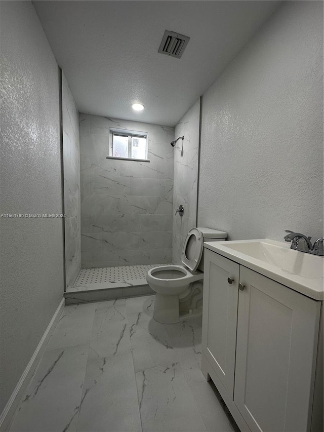 bathroom featuring a tile shower, vanity, and toilet