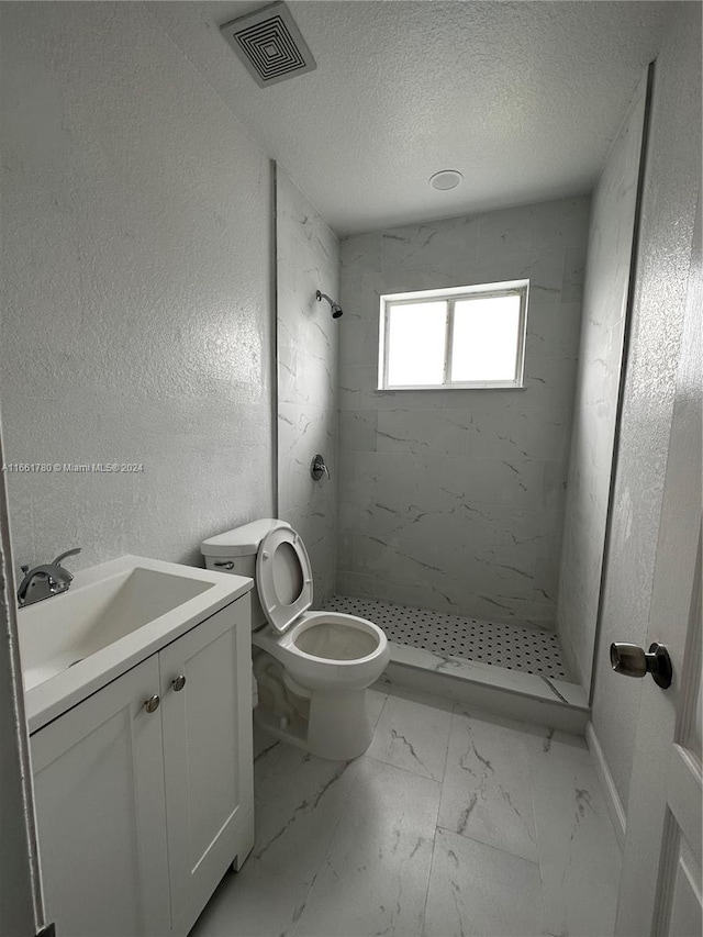 bathroom with vanity, toilet, a textured ceiling, and tiled shower