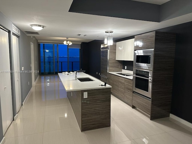 kitchen featuring appliances with stainless steel finishes, a center island with sink, light tile patterned floors, and decorative light fixtures