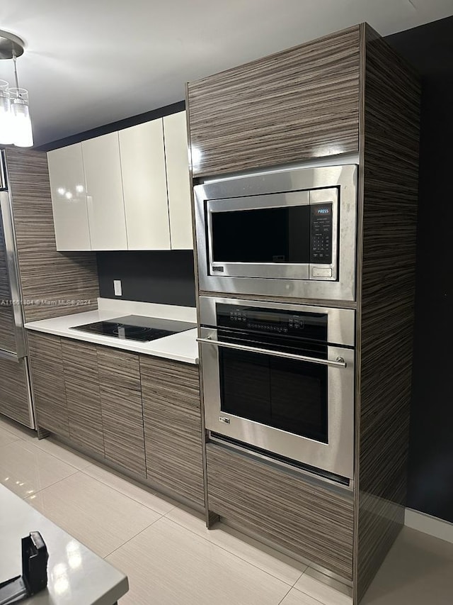 kitchen featuring hanging light fixtures, light tile patterned floors, backsplash, white cabinetry, and appliances with stainless steel finishes