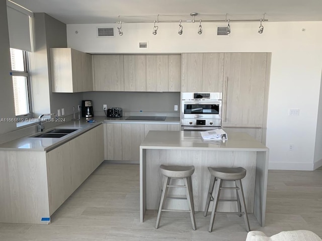 kitchen featuring stainless steel double oven, light wood-type flooring, a kitchen island, and sink