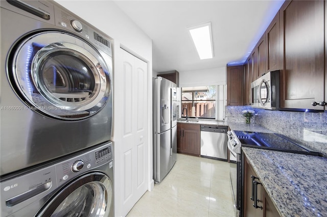 laundry area featuring sink, light tile patterned floors, and stacked washer and clothes dryer