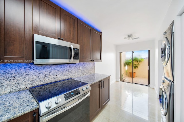 kitchen with dark brown cabinets, stacked washer and dryer, light stone counters, backsplash, and appliances with stainless steel finishes