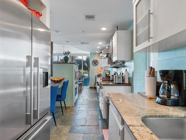 kitchen featuring stainless steel appliances, light stone countertops, white cabinets, and backsplash