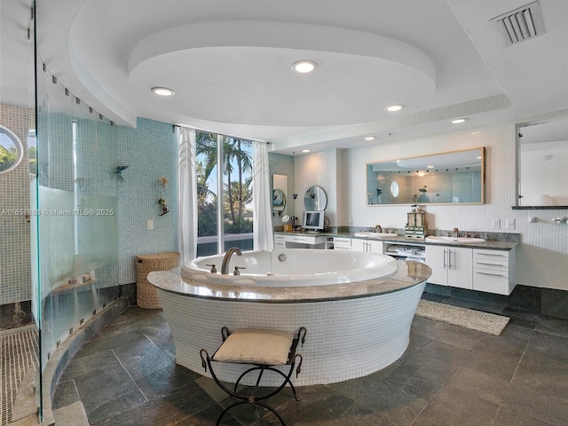 bathroom featuring vanity, a tray ceiling, independent shower and bath, and tile walls