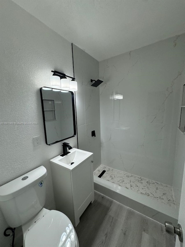 bathroom featuring a tile shower, vanity, toilet, and hardwood / wood-style flooring