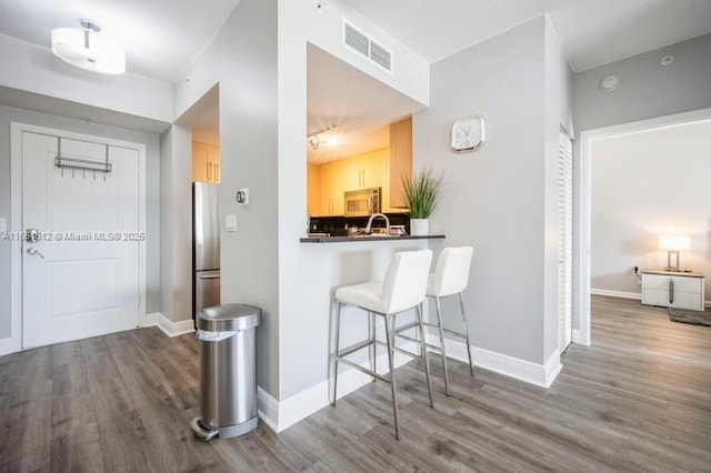 kitchen featuring hardwood / wood-style floors, light brown cabinets, a breakfast bar area, kitchen peninsula, and stainless steel appliances