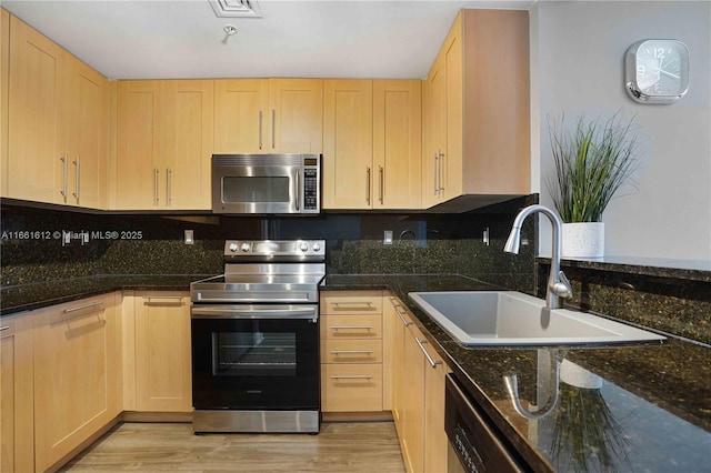 kitchen with appliances with stainless steel finishes, dark stone counters, light brown cabinetry, sink, and light wood-type flooring