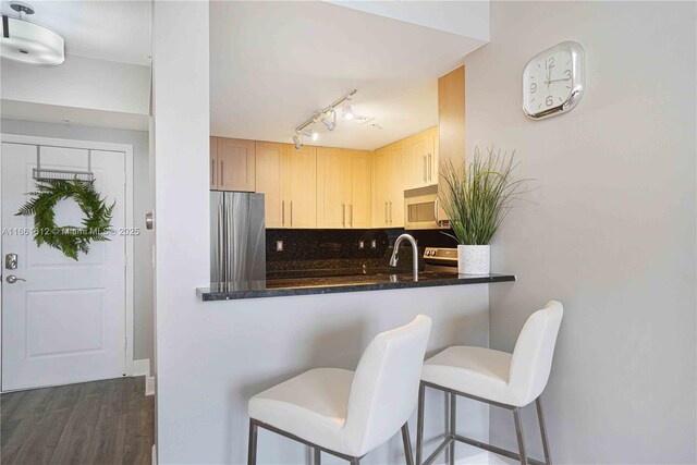 kitchen with light brown cabinets, backsplash, stainless steel fridge, kitchen peninsula, and a breakfast bar