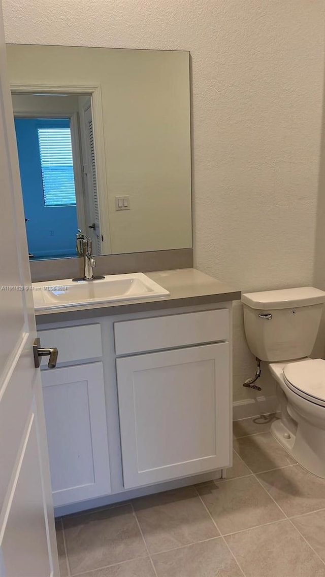 half bathroom with toilet, tile patterned flooring, and vanity